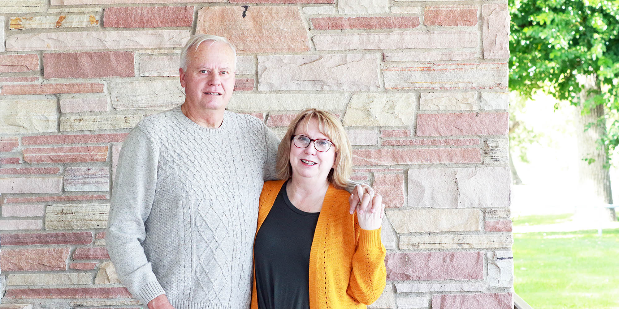 Jesse and Sandy Pape hold hands as they pose in front of a Colorado sandstone building.