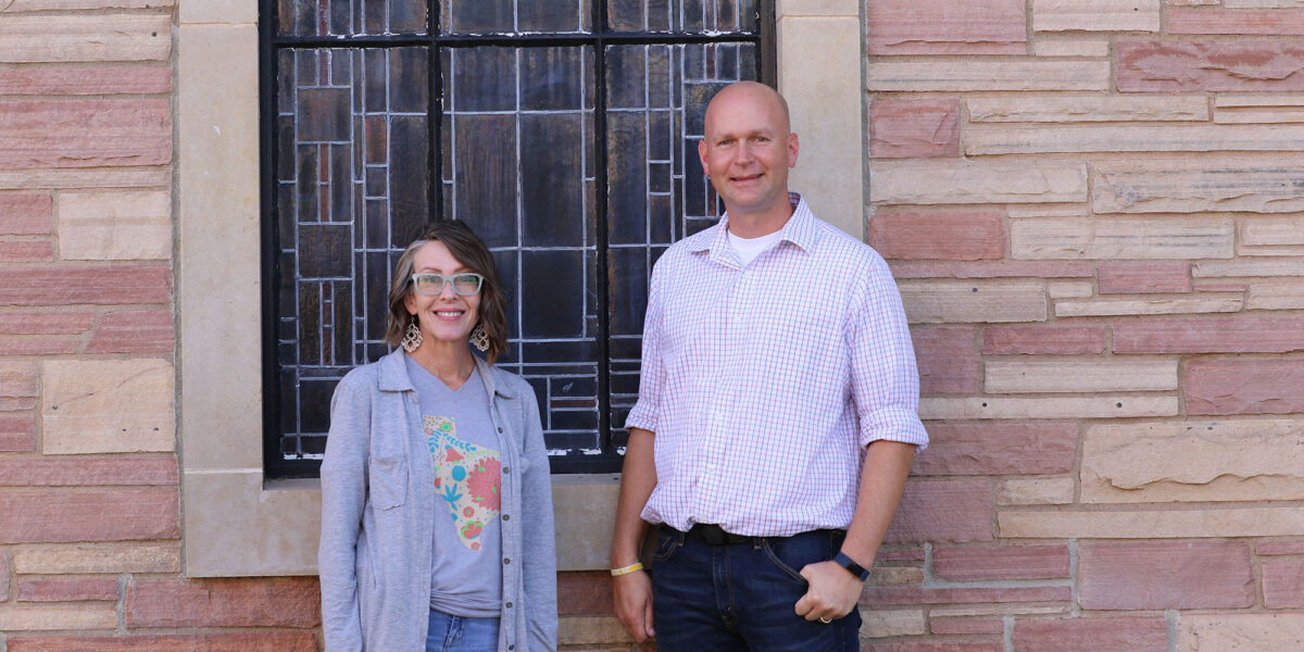 A man and a woman stand in front of a stained glass window.