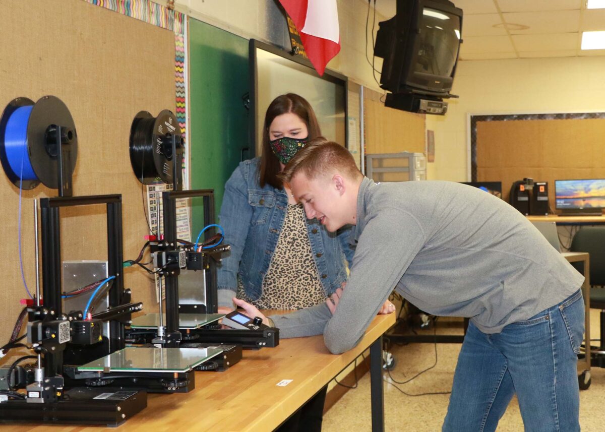 A woman and a boy look at a 3D printing setup.