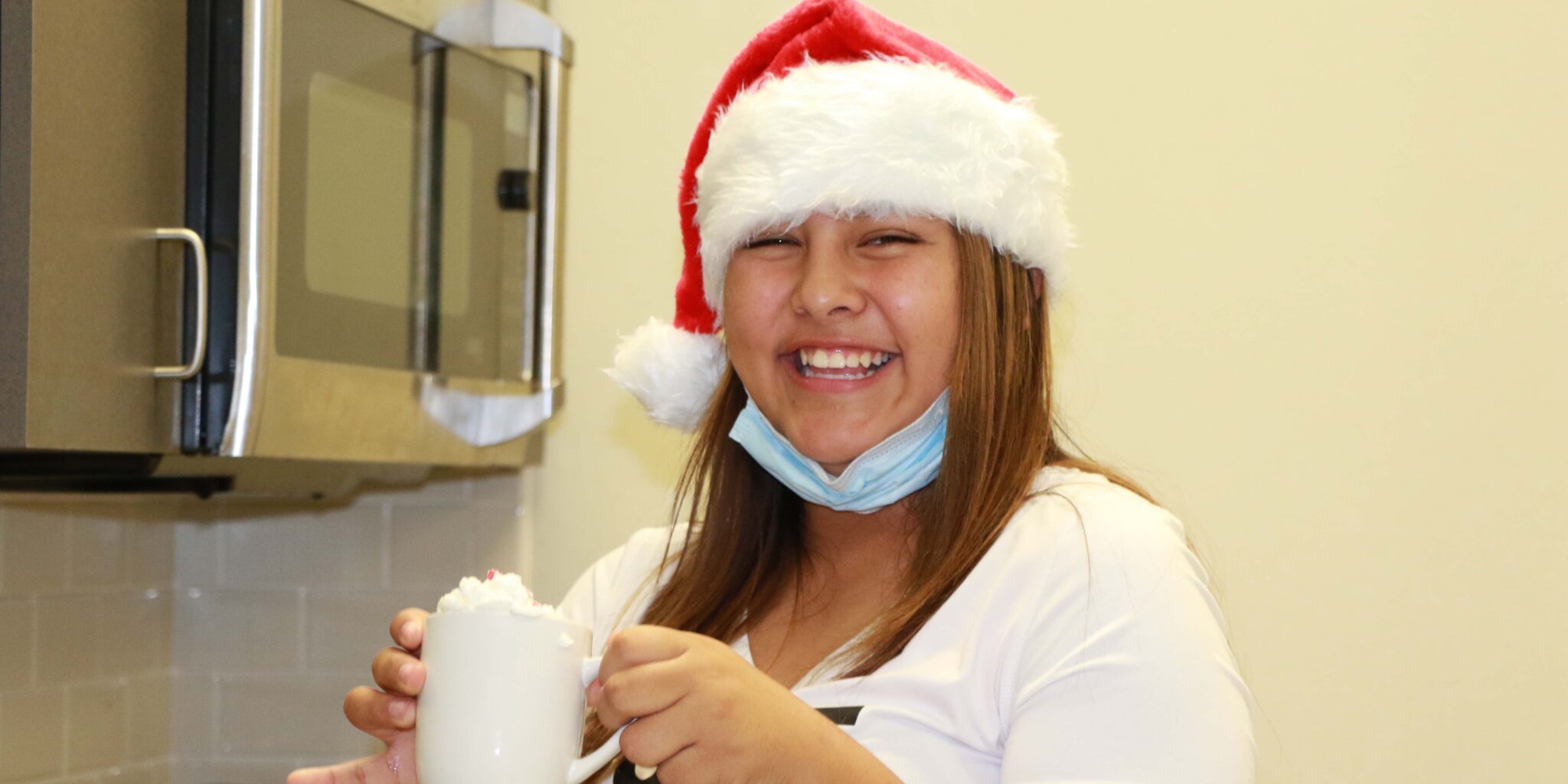 A girl in a Santa hat enjoys a mug cake.