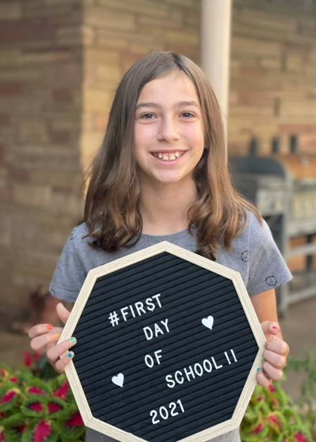 A girl holds a sign that reads "First Day of School 2021."