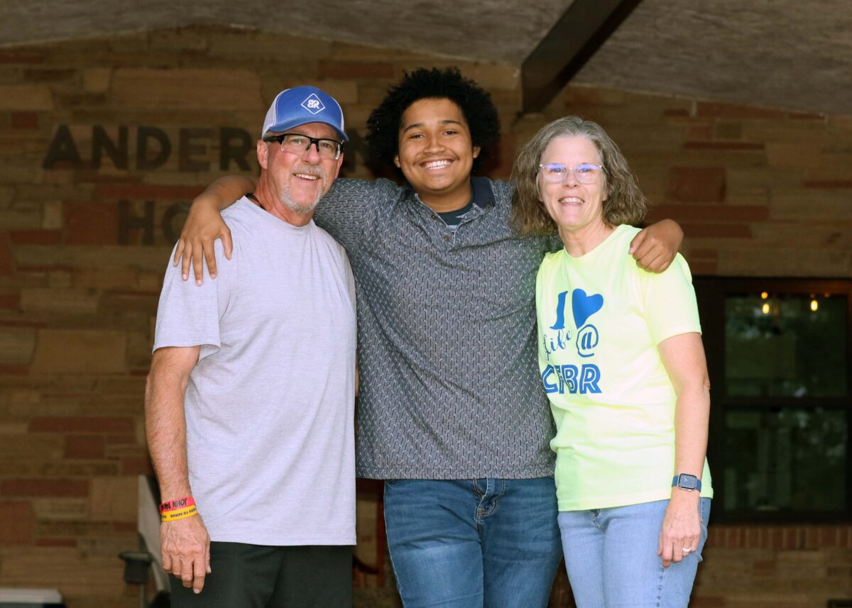 A boy stands between two adults on the steps of a group home.