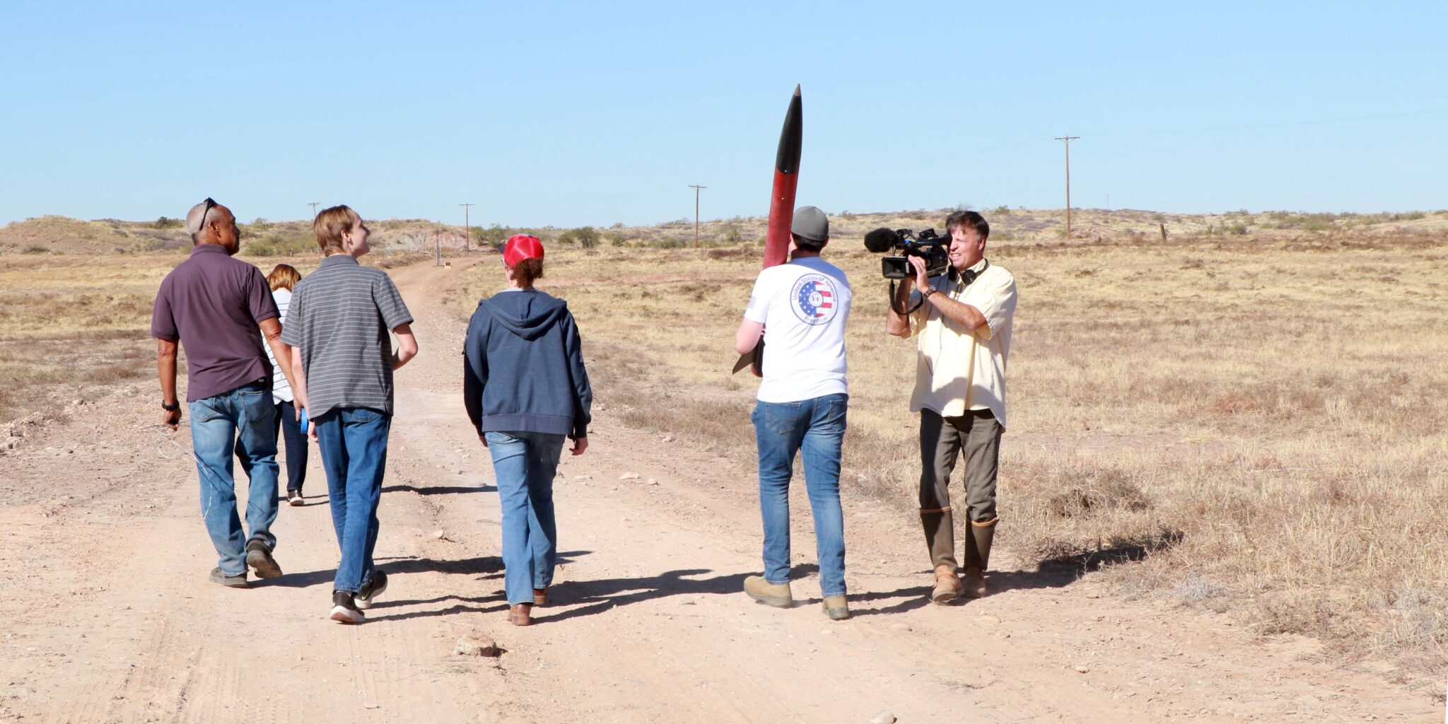 Students and a videographer carry a rocket to launch.