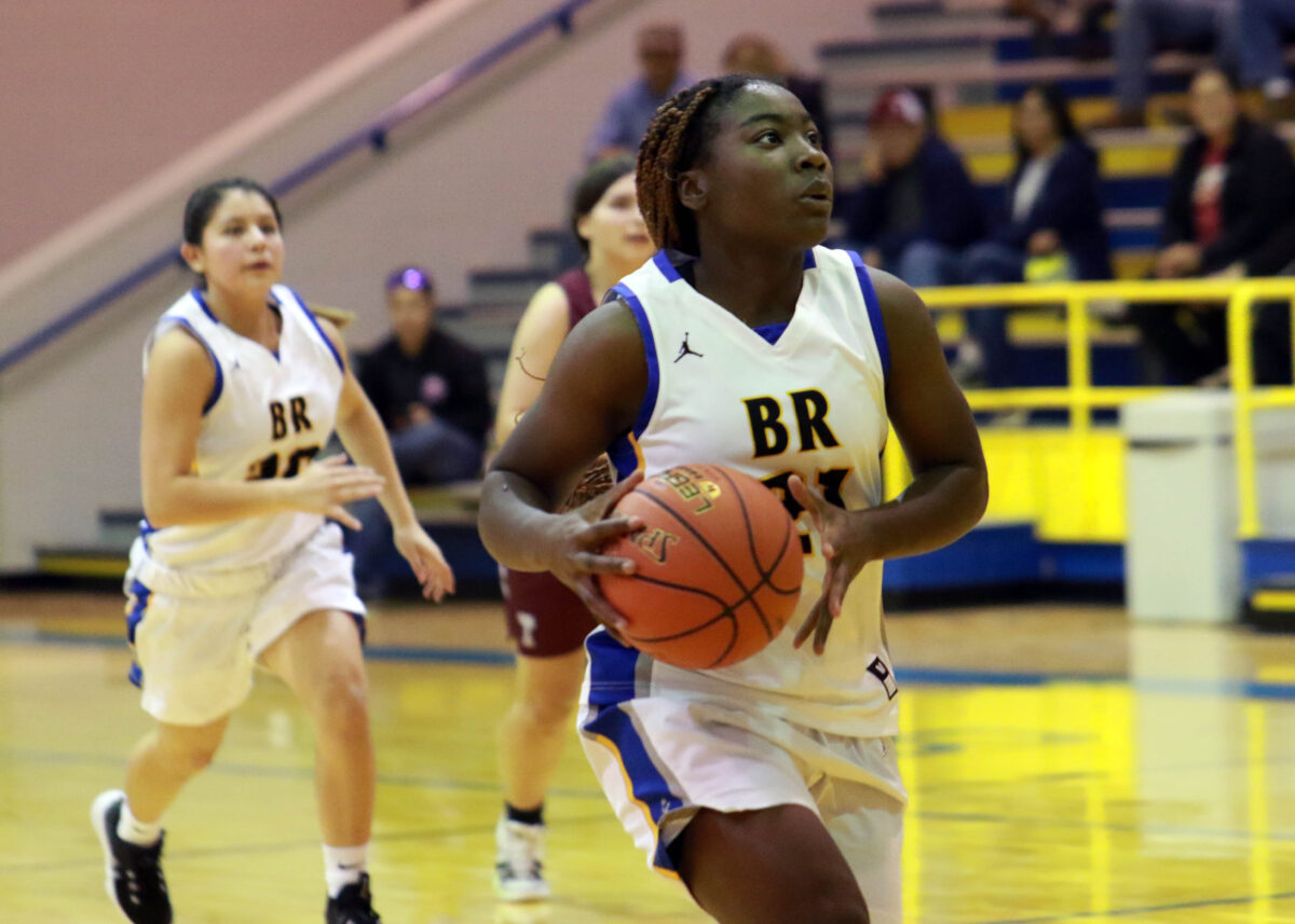 A girl playing basketball carries the ball toward the basket.