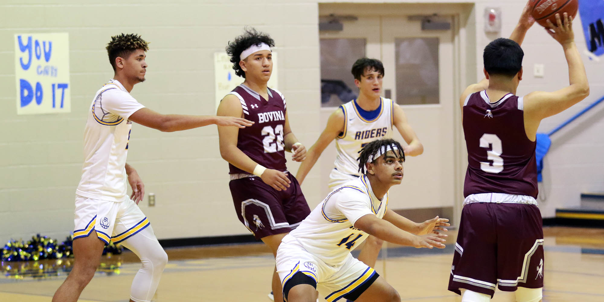 3 basketball players wearing white defend against an opponent.