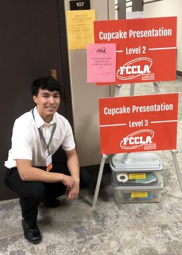 A boy kneels beside a sign showing he has competed in FCCLA events.