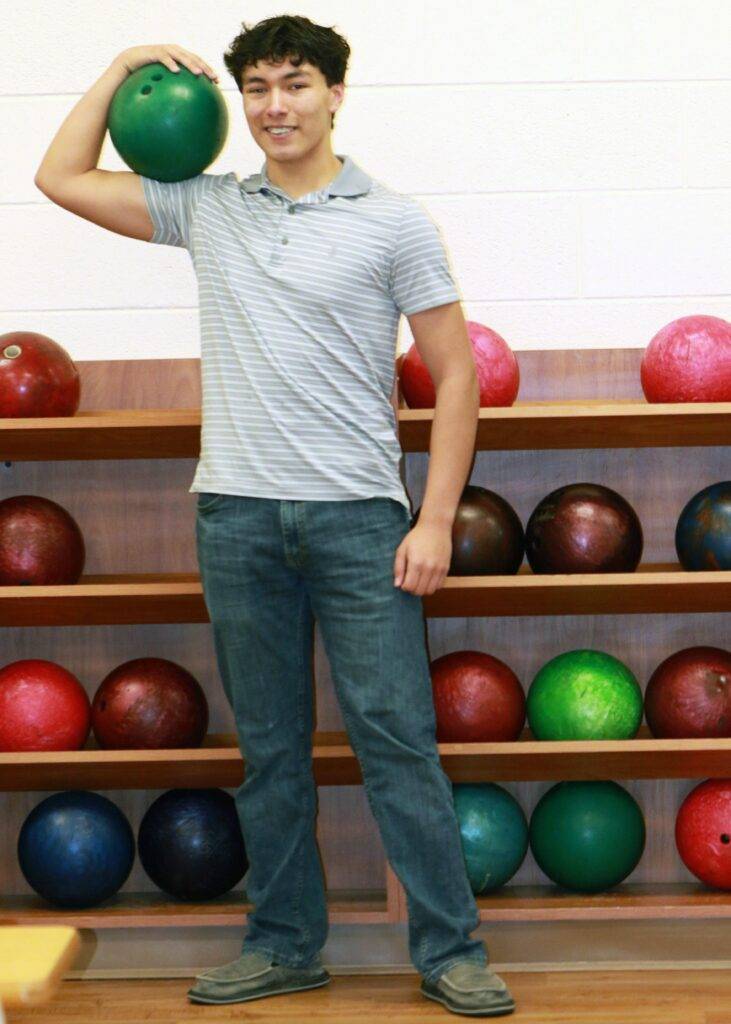 A boy holds a bowling ball on his shoulder.