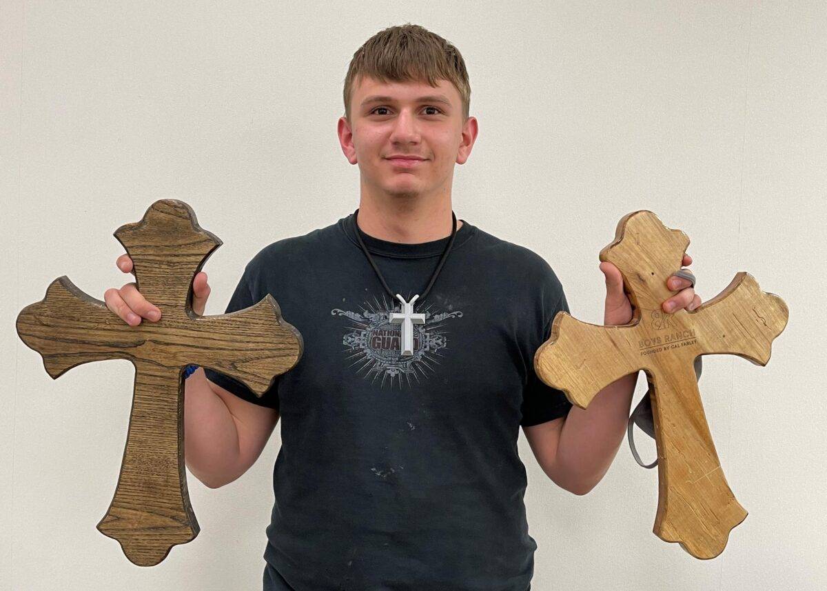 A boy holds a decorative wooden cross in each hand.