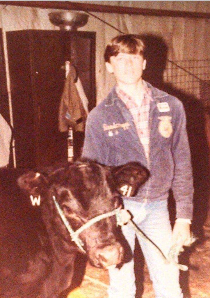 A boy in an FFA jacket leads a steer by a halter.