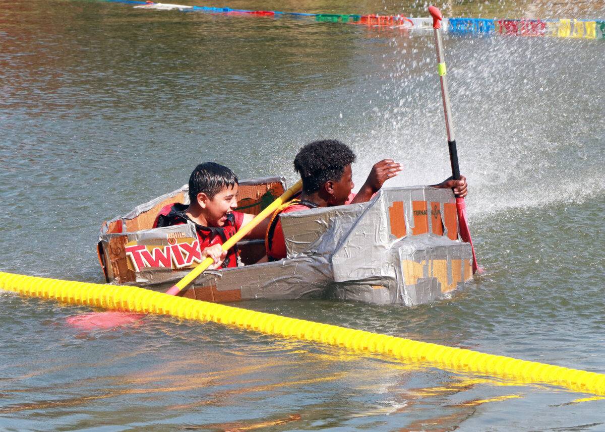 Two boys paddle a boat made of cardboard and duct tape.