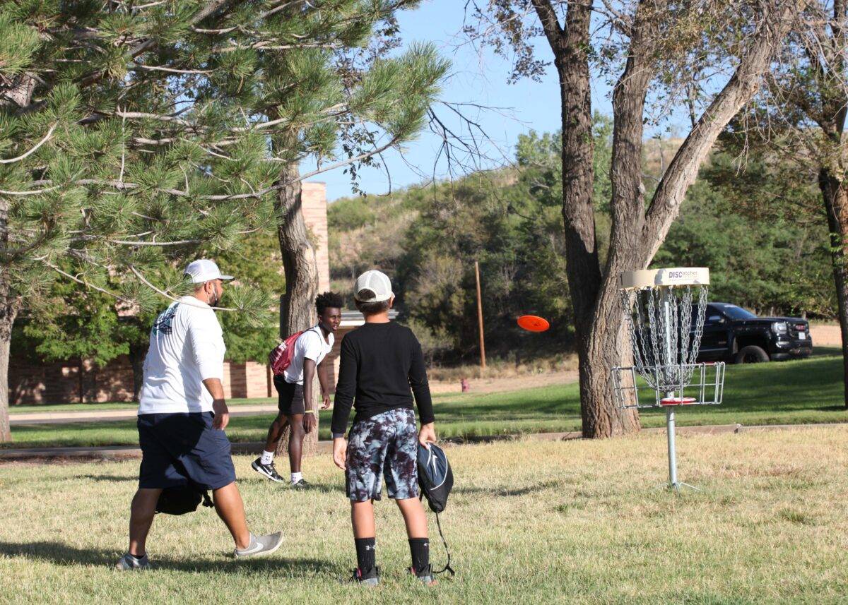 two children and an adult play disc golf.