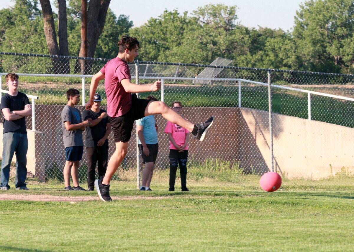 A teenager kicks a large rubber ball during a game of kickball.