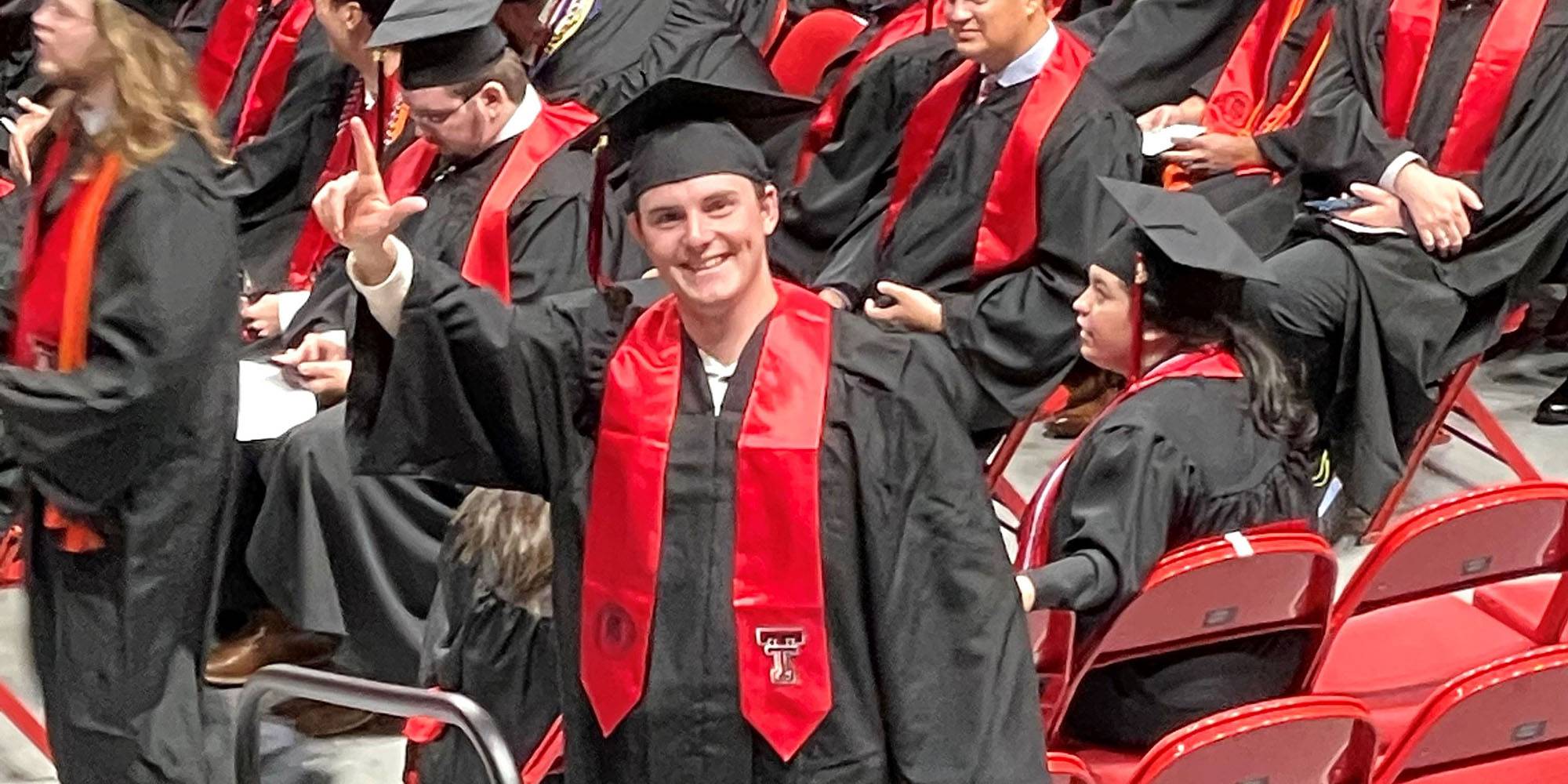 A student earing black robes with red makes a Texas Tech symbol with his hand.