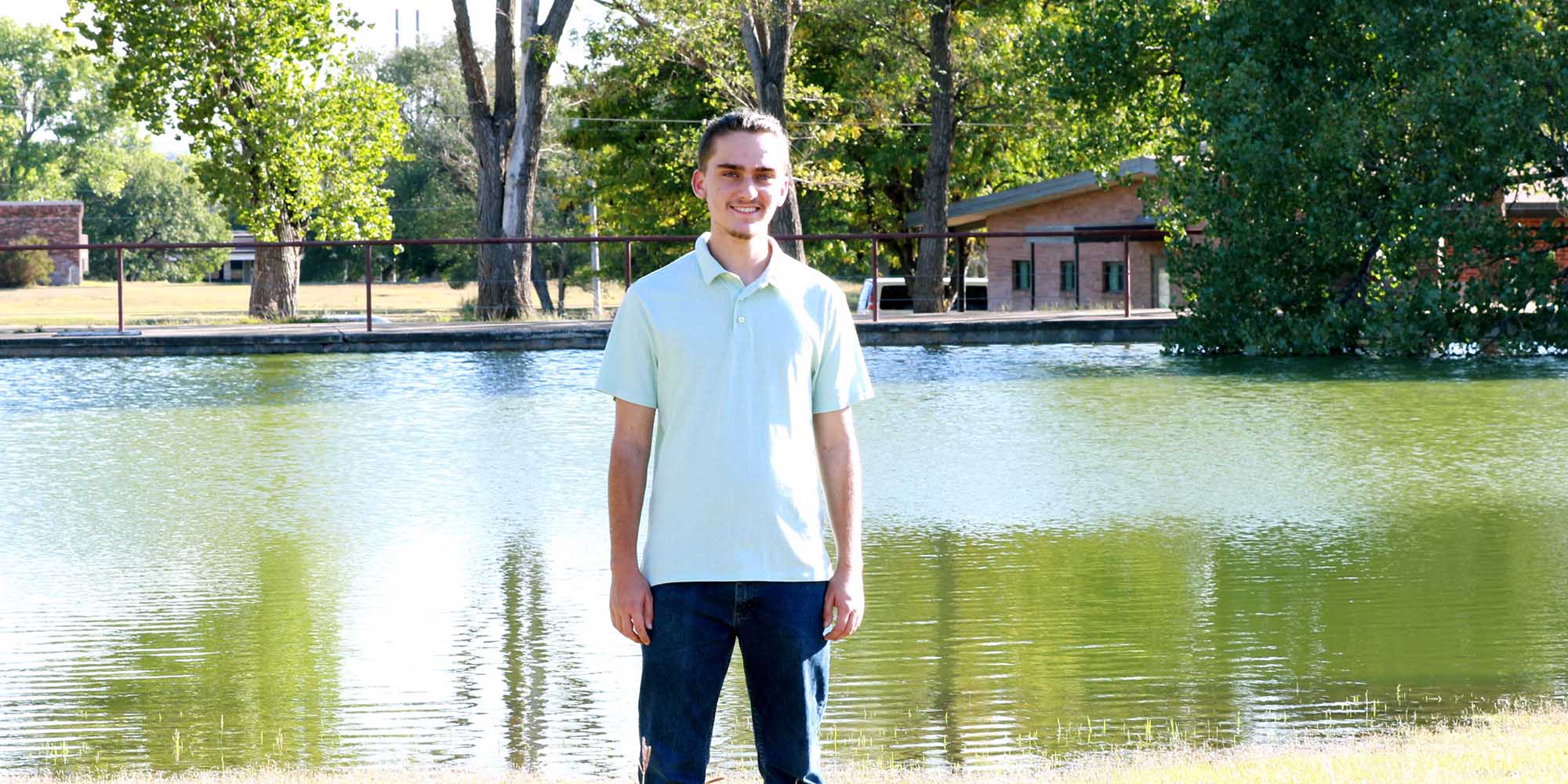 A teenager stands in front of a pond.