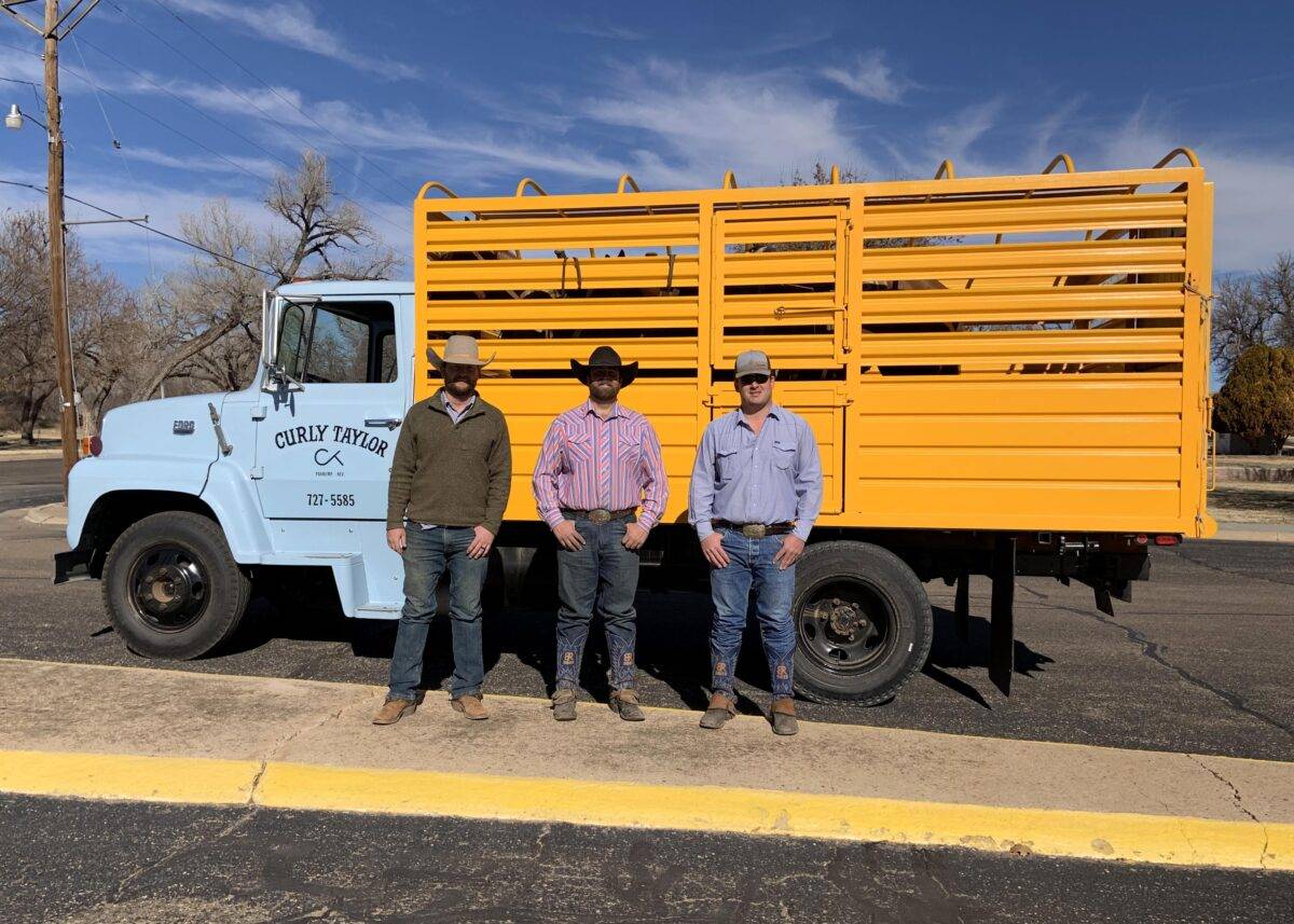 Three men stand in front of a panel truck.