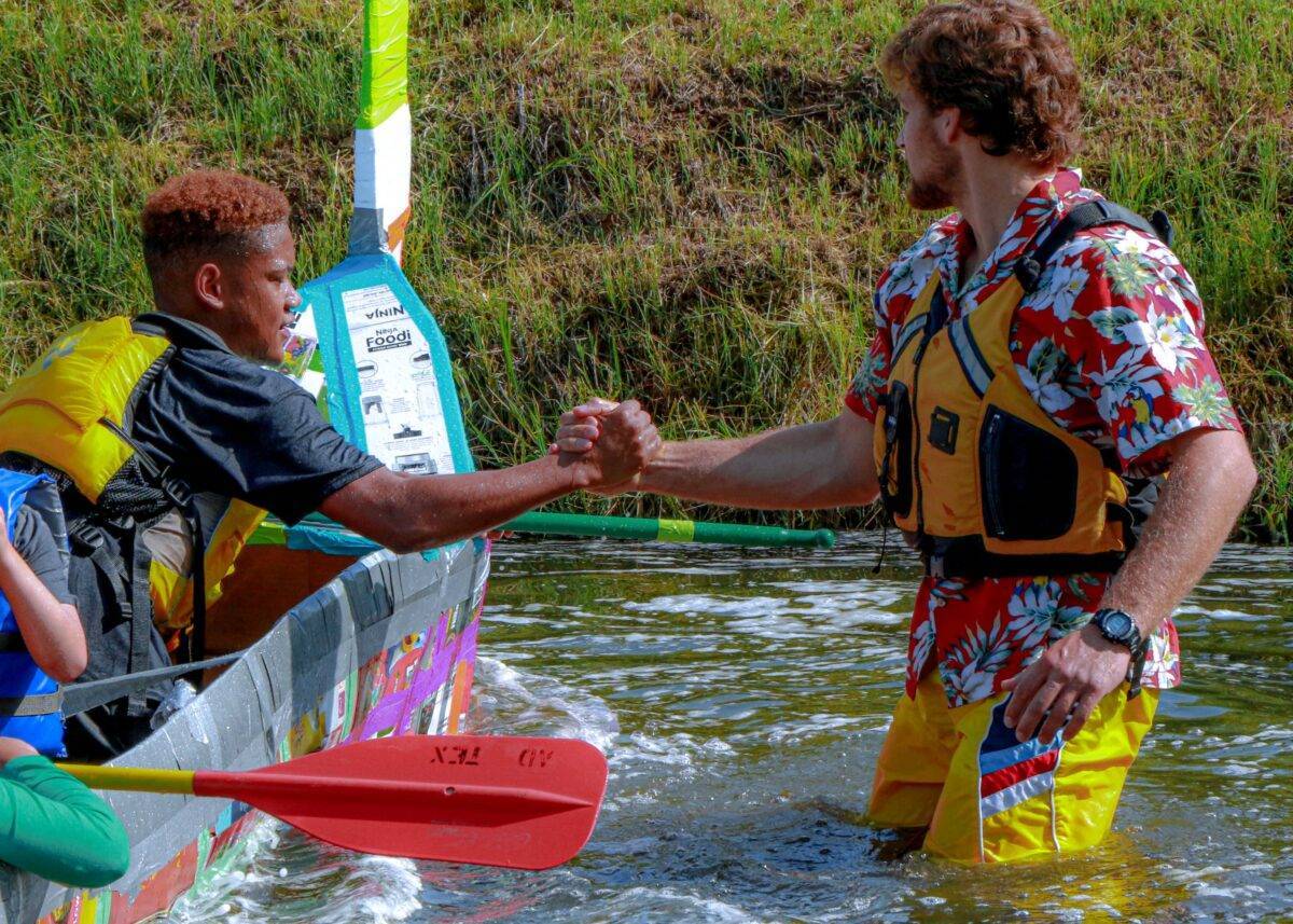 A young man holds a child's hand to help him out of the water.